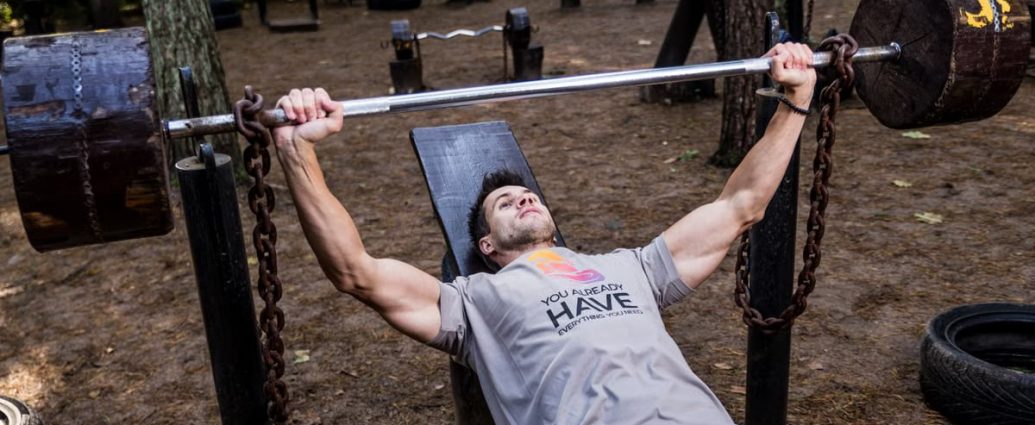 Man weightlifting outdoors, using a bench press setup amid trees for strength training.