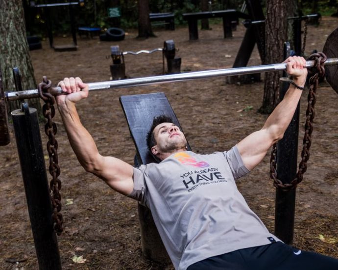 Man weightlifting outdoors, using a bench press setup amid trees for strength training.