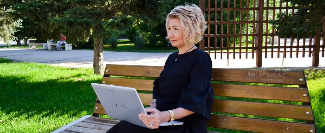 Woman sitting on a bench with a laptop, enjoying a sunny day in a green park setting.